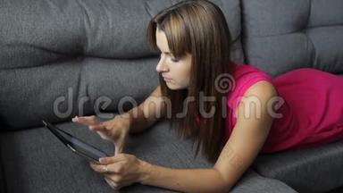 穿裙子<strong>的女人躺在沙发上的</strong>平板电脑<strong>上</strong>。 趴<strong>在</strong>肚子<strong>上</strong>.. 可爱<strong>的女人在</strong>家
